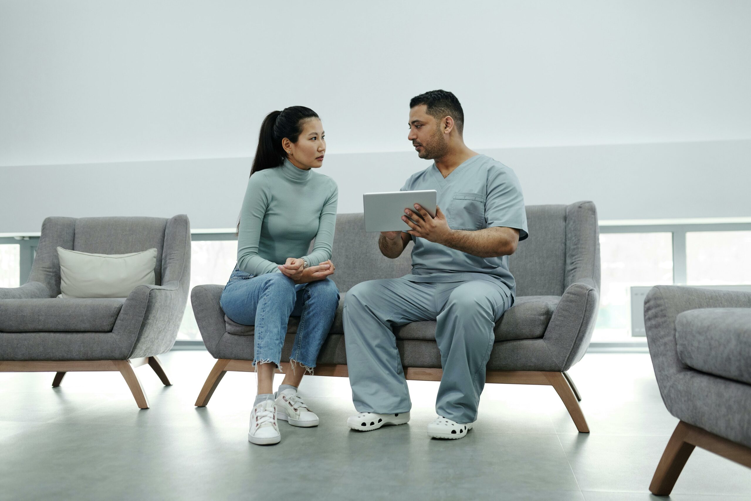 nurse in gray scrubs speaking with a patient on a couch
